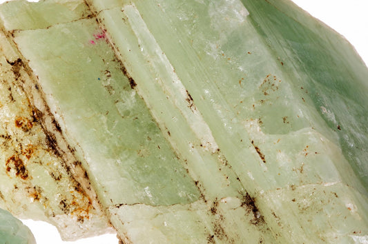 A close-up of a raw aquamarine crystal showing pale green, translucent facets with brown and white mineral inclusions on a dark surface.