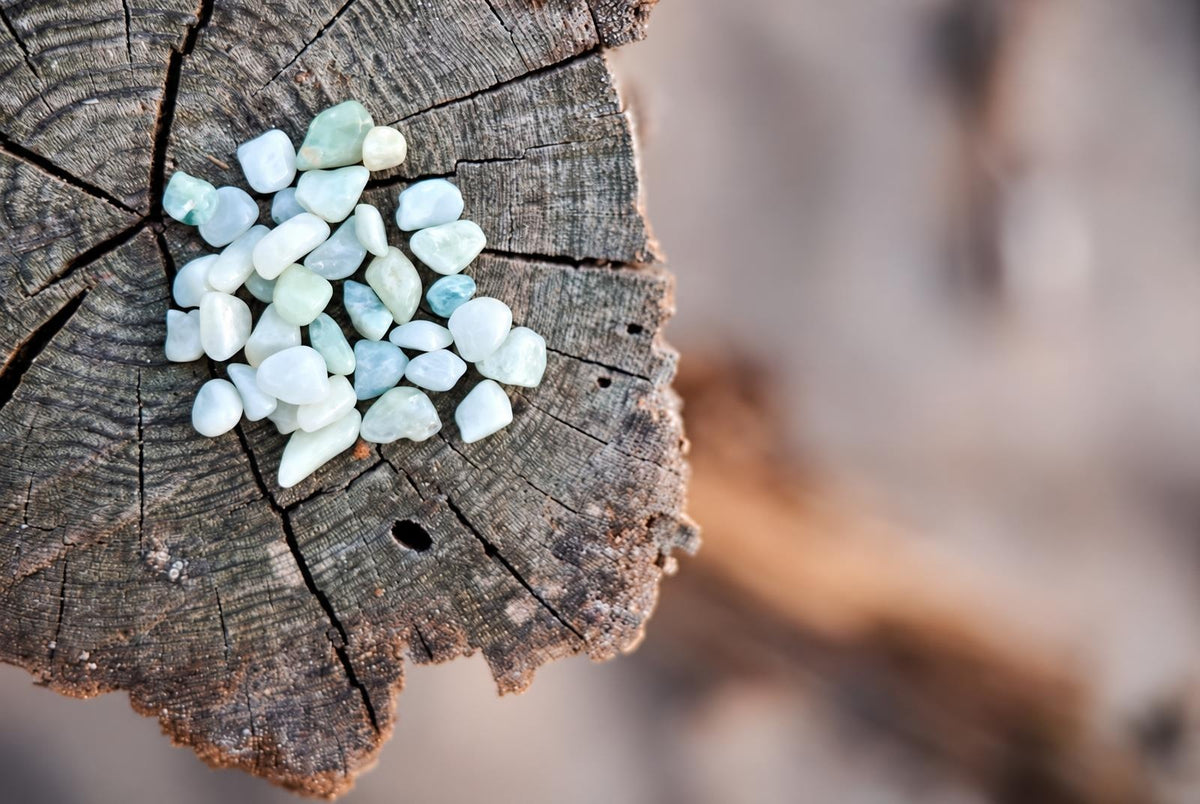 A pile of small, smooth aquamarine stones in pale blue and white rests on a dark wooden surface.