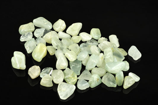 A pile of small, smooth stones in pale green and white tones on a dark surface.