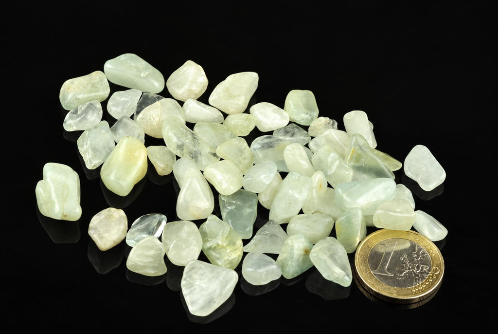 A pile of pale green and white rough stones on a dark surface, with a one euro coin for scale.