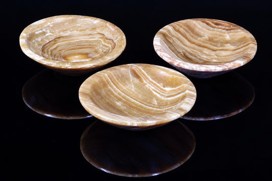 Three shallow bowls with swirling brown and cream banding sit on a dark, reflective surface.