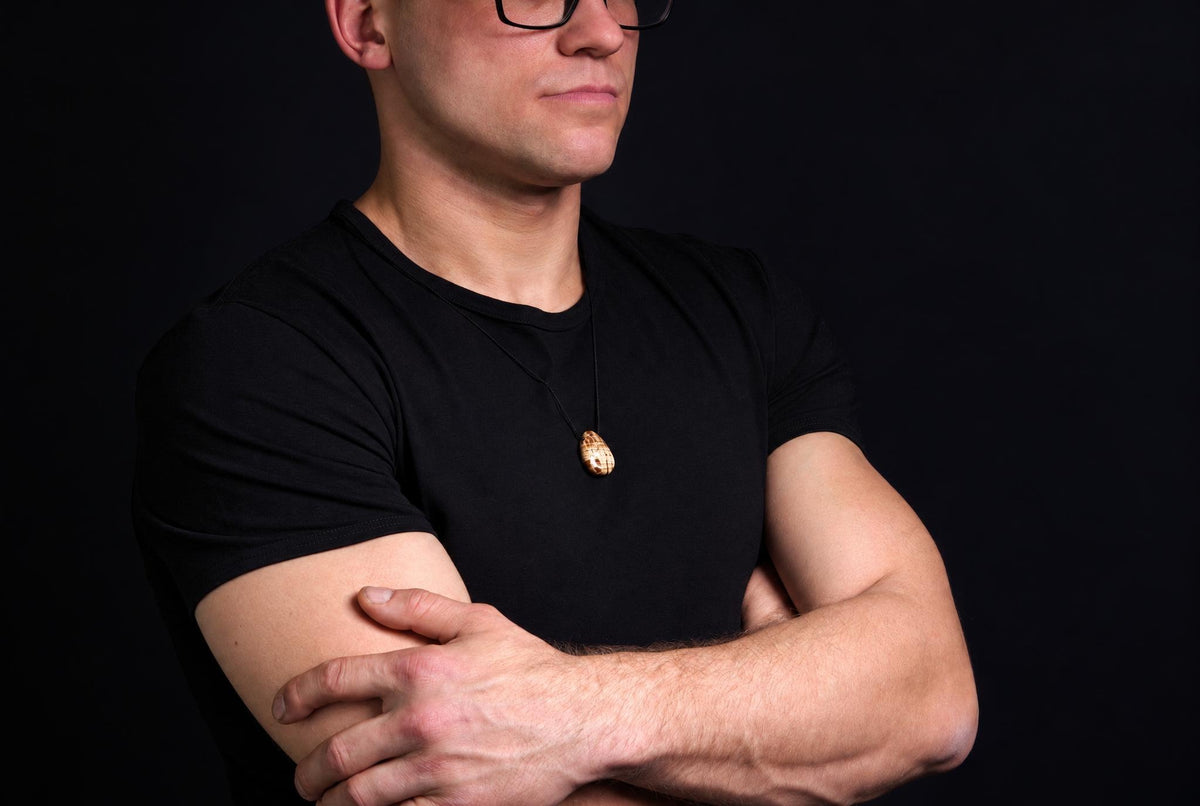A man in a black t-shirt wears an oval pendant with light and dark brown patterns on a dark surface.