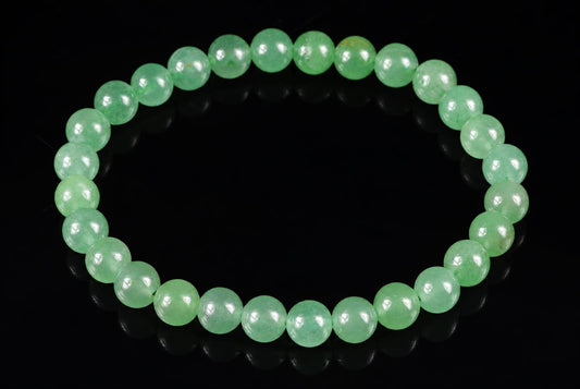 A bracelet of round, light green aventurine beads arranged in a circle on a dark surface.