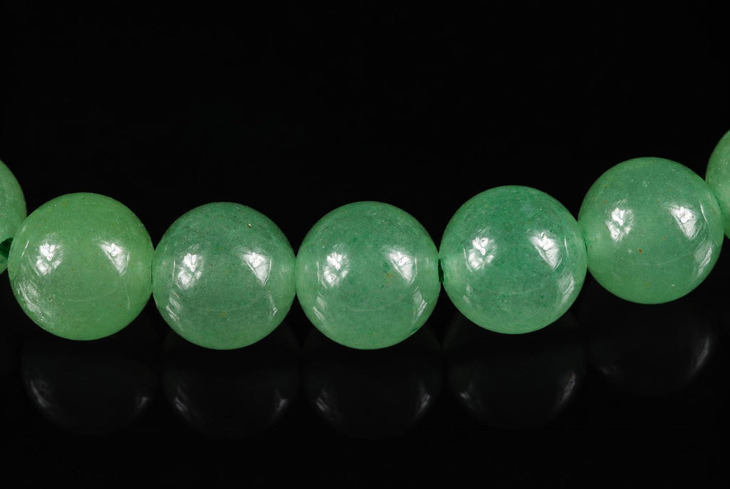A row of round, light green aventurine beads on a dark surface with reflections.