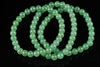 A bracelet of round, light green aventurine beads arranged in loops on a dark surface.