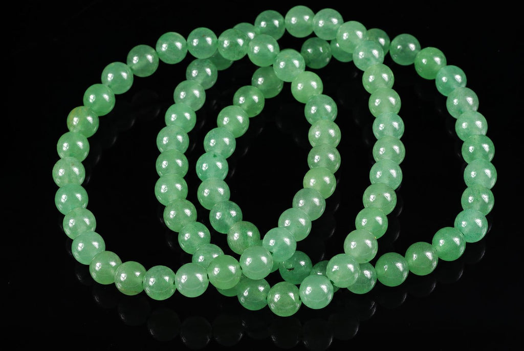 A bracelet of round, light green aventurine beads arranged in loops on a dark surface.
