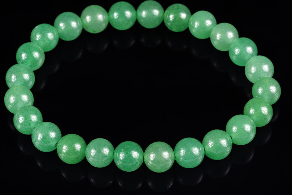 A bracelet of round, light green aventurine beads arranged in a circle on a dark surface.
