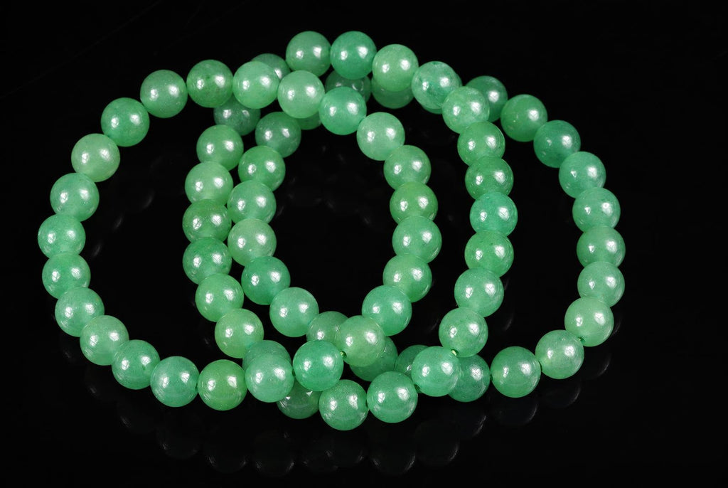 A green Aventurine bracelet with round beads arranged in loops on a dark surface.