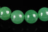 Four round green aventurine beads with golden flecks on a dark surface.