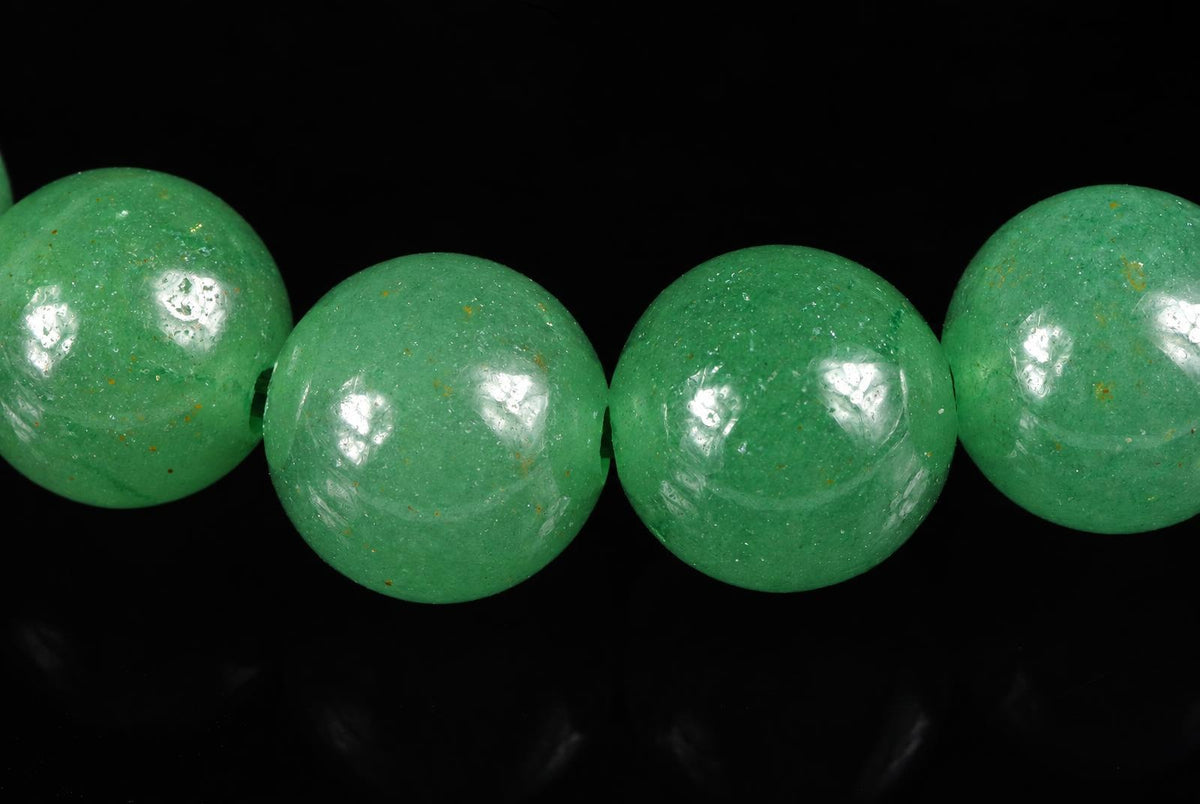 Four round green aventurine beads with golden flecks on a dark surface.