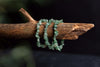 Three light green aventurine chip bracelets rest on a rough wooden branch against a dark background.