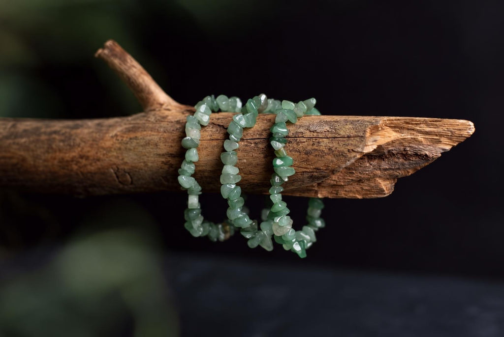 Three light green aventurine chip bracelets rest on a rough wooden branch against a dark background.