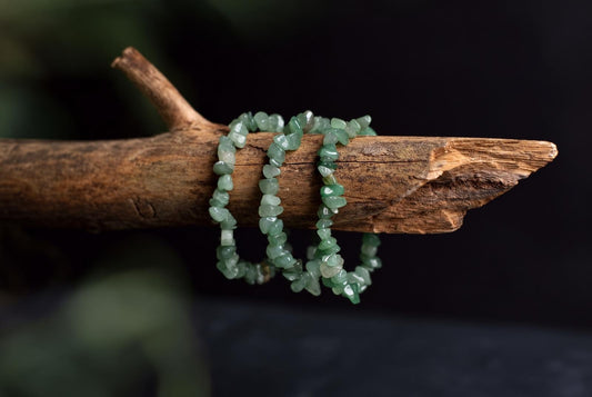Three light green aventurine chip bracelets rest on a rough wooden branch against a dark background.