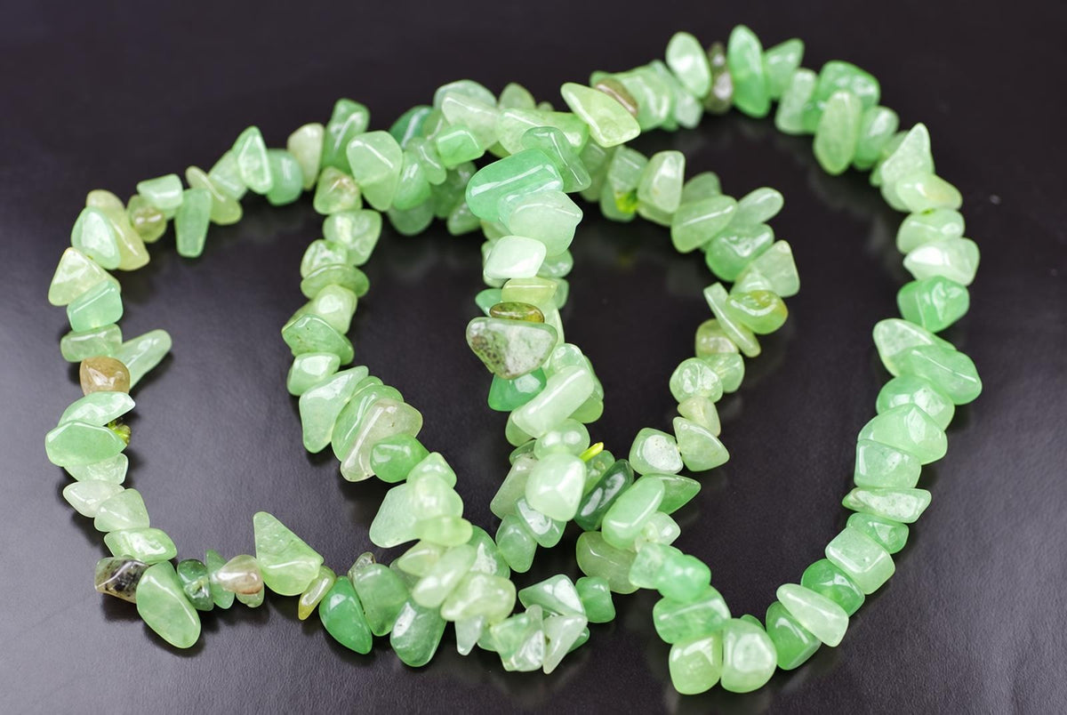 A bracelet made of irregular green aventurine chips arranged in a loose coil on a dark surface.
