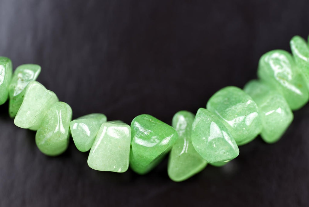 A strand of polished, light green aventurine chips arranged in a curved line on a dark surface.