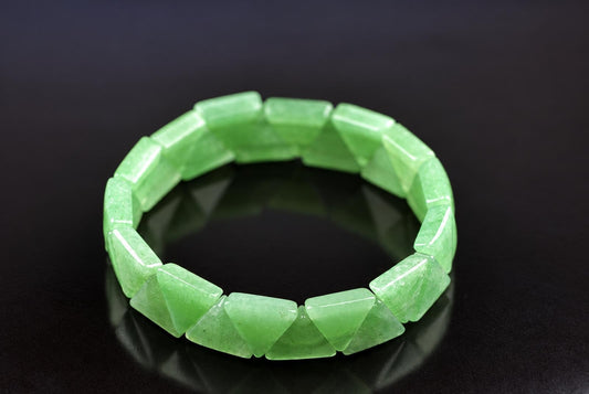 A green aventurine bracelet with triangular facets rests on a dark surface.