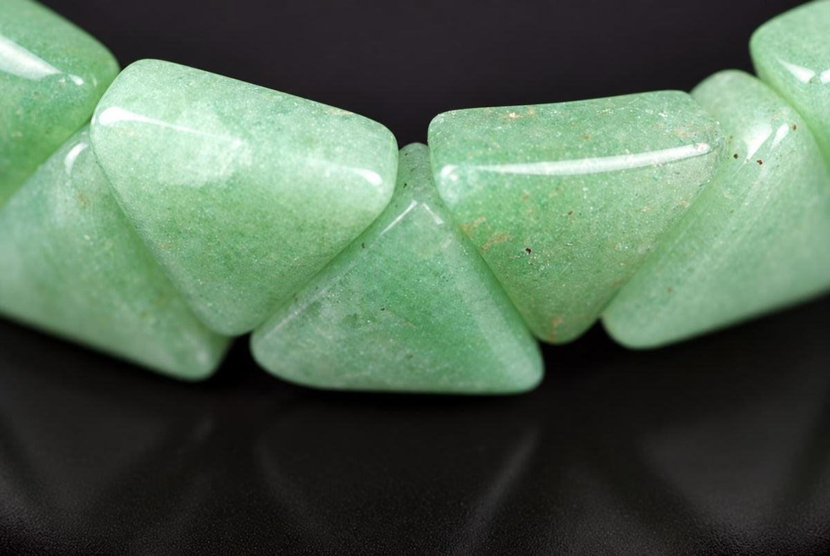 A close-up of a bracelet with light green, triangular aventurine beads on a dark surface.