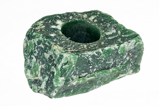 A green and white speckled stone object with a central hole, set against a plain white background.