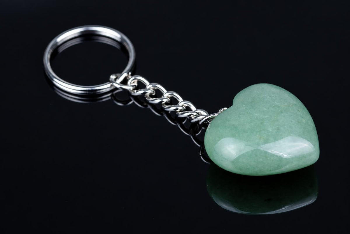 A silver-toned keychain with a polished, light green heart-shaped pendant on a dark reflective surface.