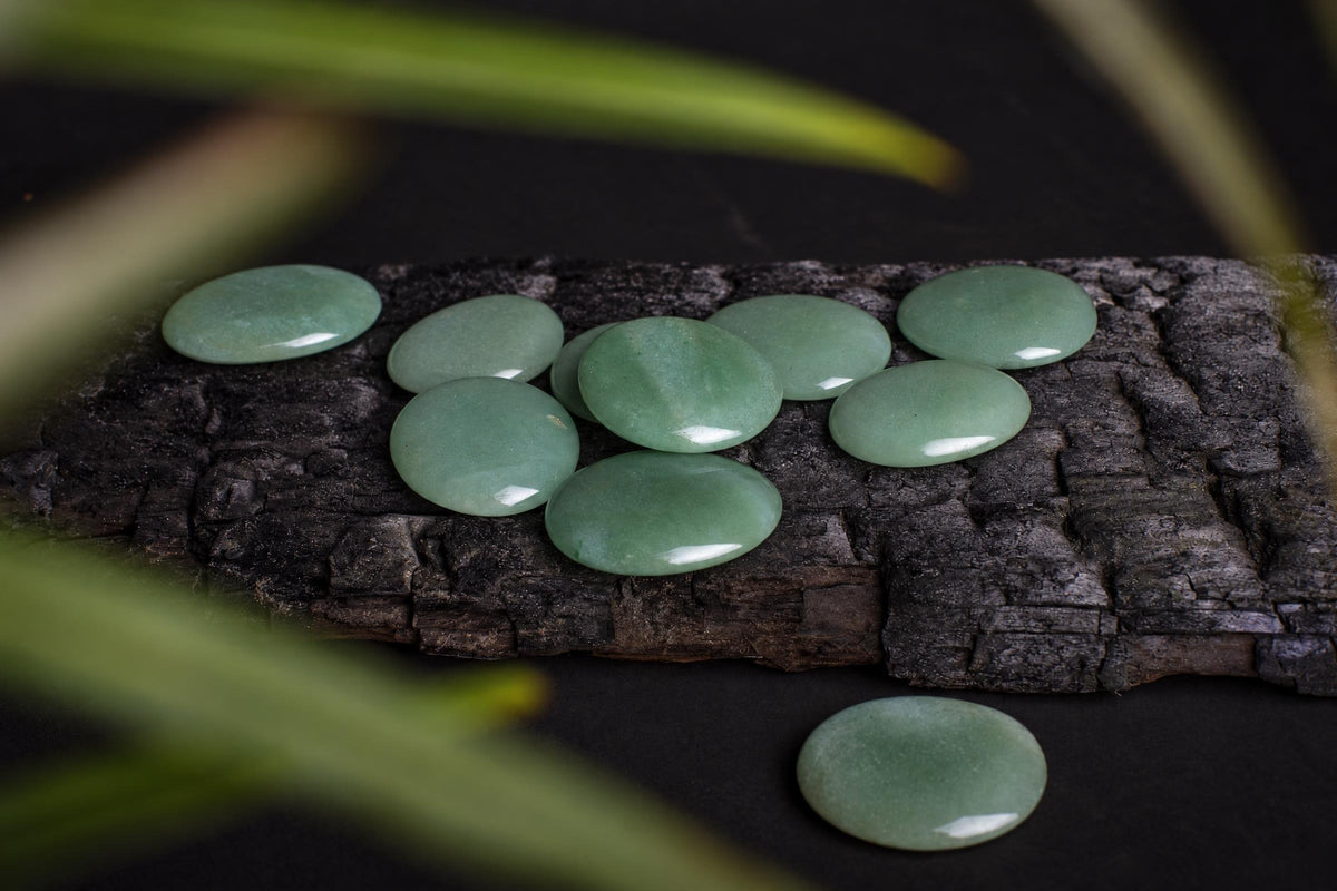 Several smooth, pale green oval stones rest on a dark wooden surface with blurred green leaves in the foreground.