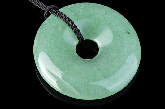 A round, light green aventurine pendant with a central hole and a dark cord against a black background.