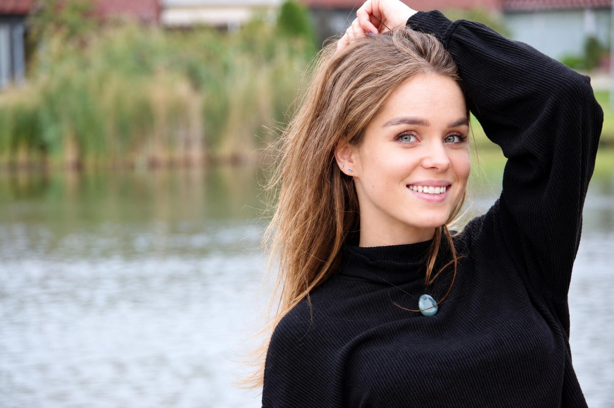 A woman wears a black turtleneck sweater with a smooth, pale green Aventurine pendant on a thin cord.