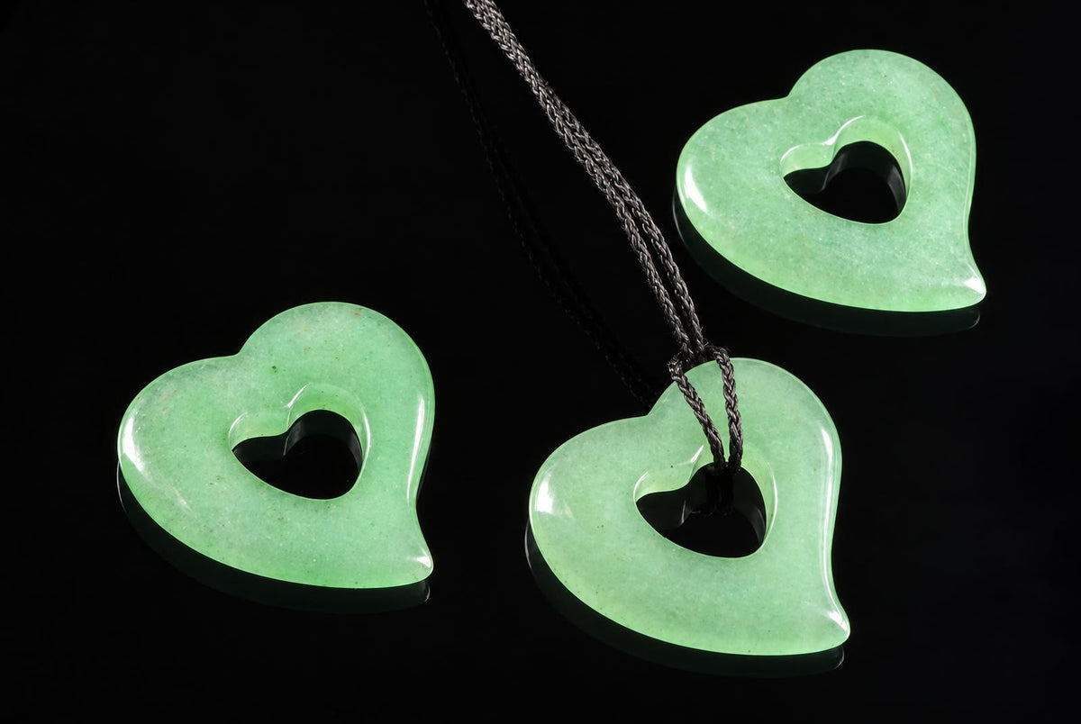 Three light green heart-shaped pendants with dark inner cutouts on a black surface; one hangs from a braided cord.