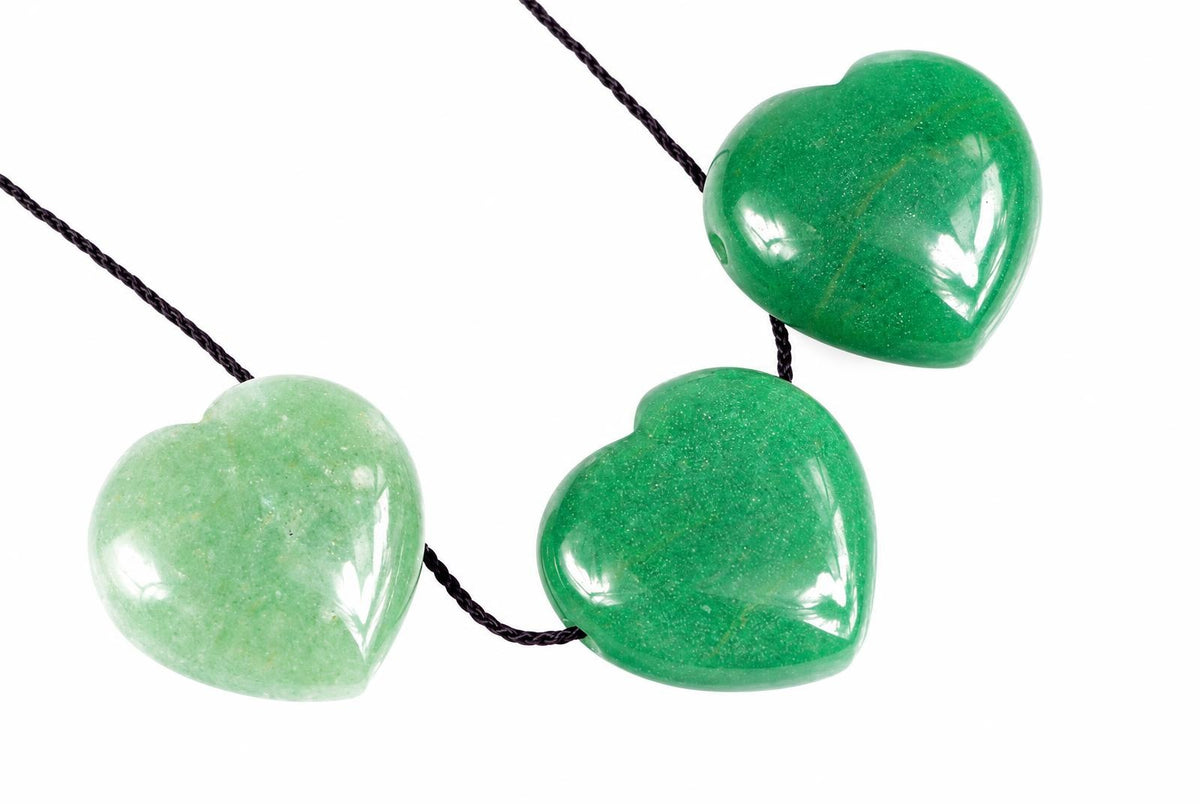 Three polished heart-shaped pendants in light and dark green tones hang on a black cord against a white background.