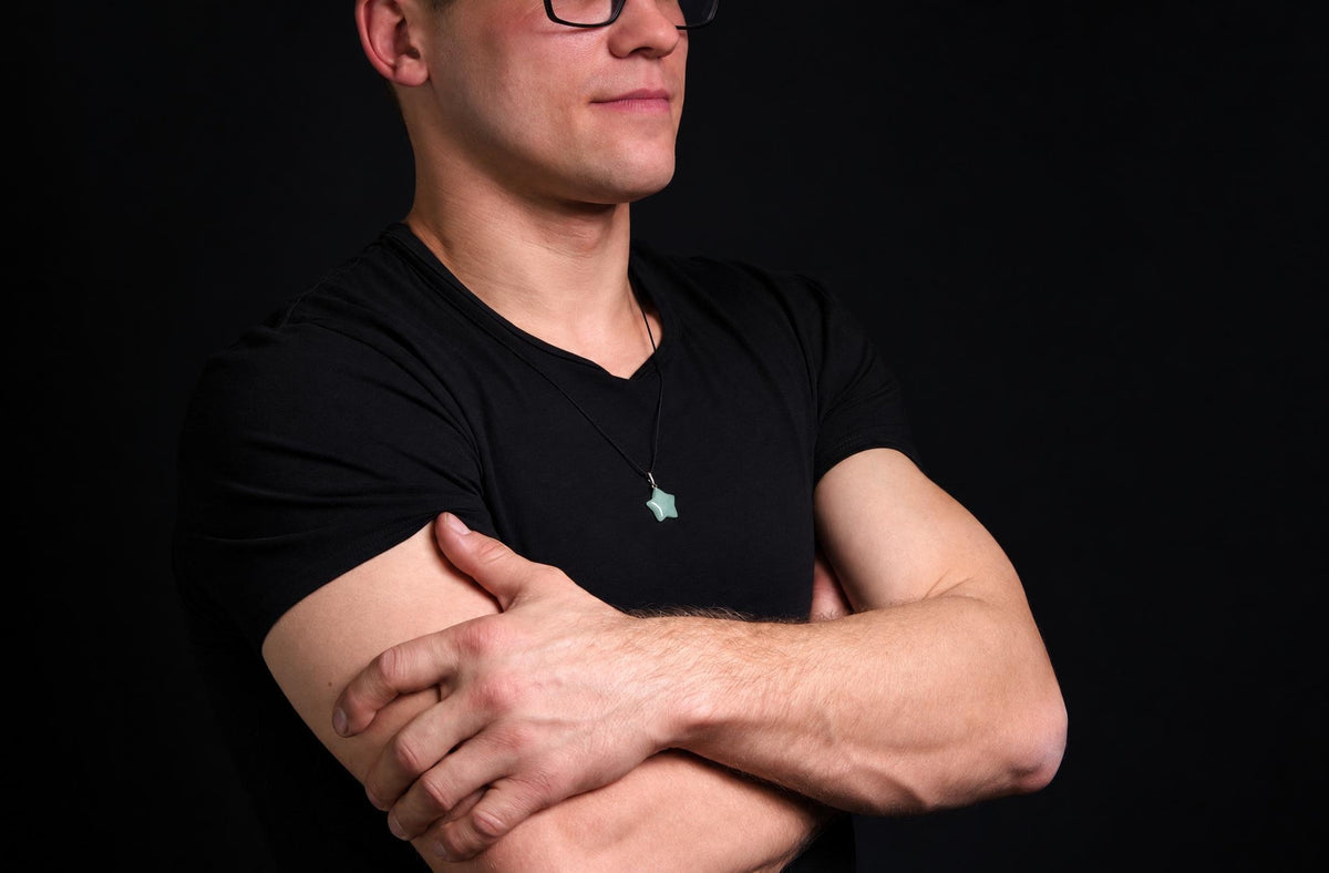 A man in a black t-shirt wears a star-shaped pendant on a dark surface.