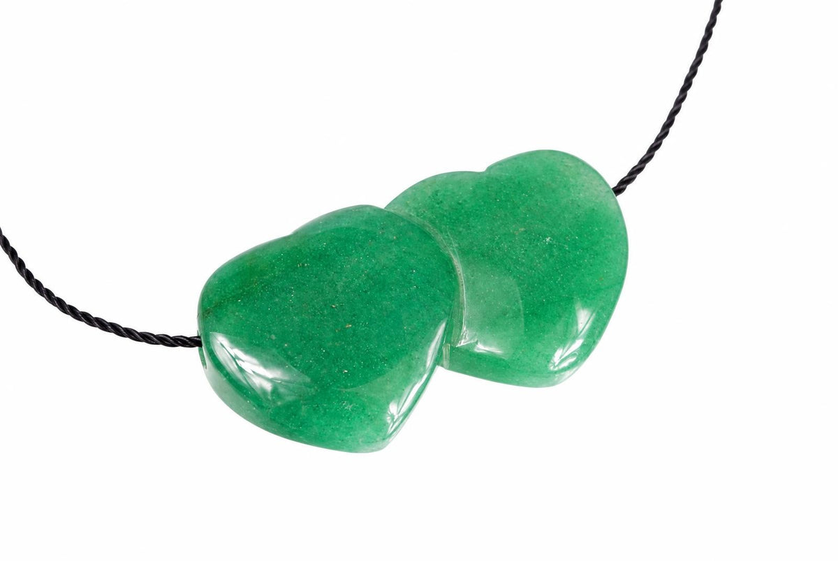A green aventurine pendant shaped like two joined hearts on a black cord, set against a white background.