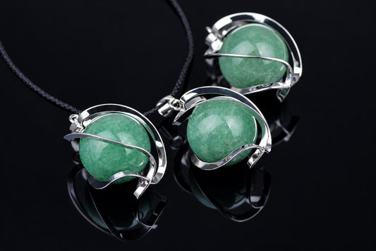 Three silver-toned pendants with round green aventurine spheres on a black cord, arranged on a dark reflective surface.