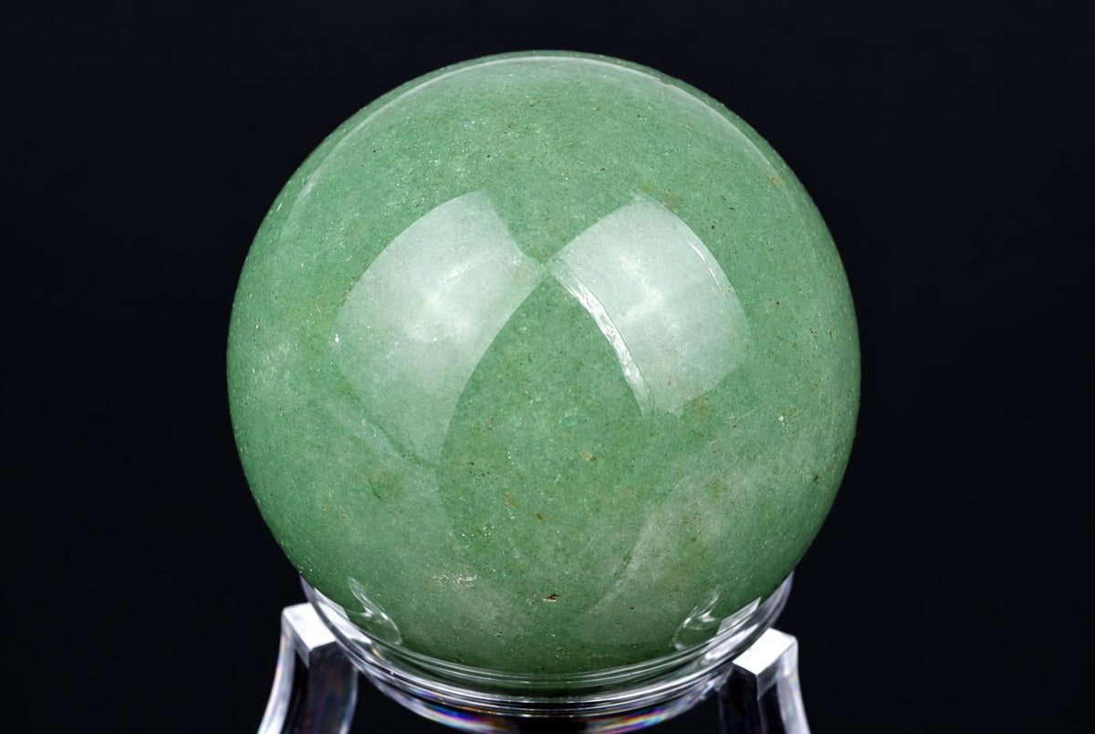 A polished green aventurine sphere rests on a clear stand against a dark background.