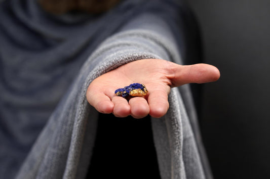 An open hand holds a small rough blue and brown azurite specimen against a softly blurred background.
