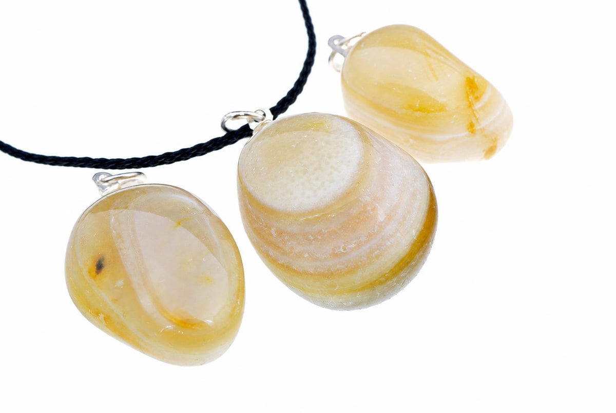 Three polished pebble-shaped pendants with banded yellow, cream and white patterns hang from silver-toned loops on a dark cord against a pale surface.