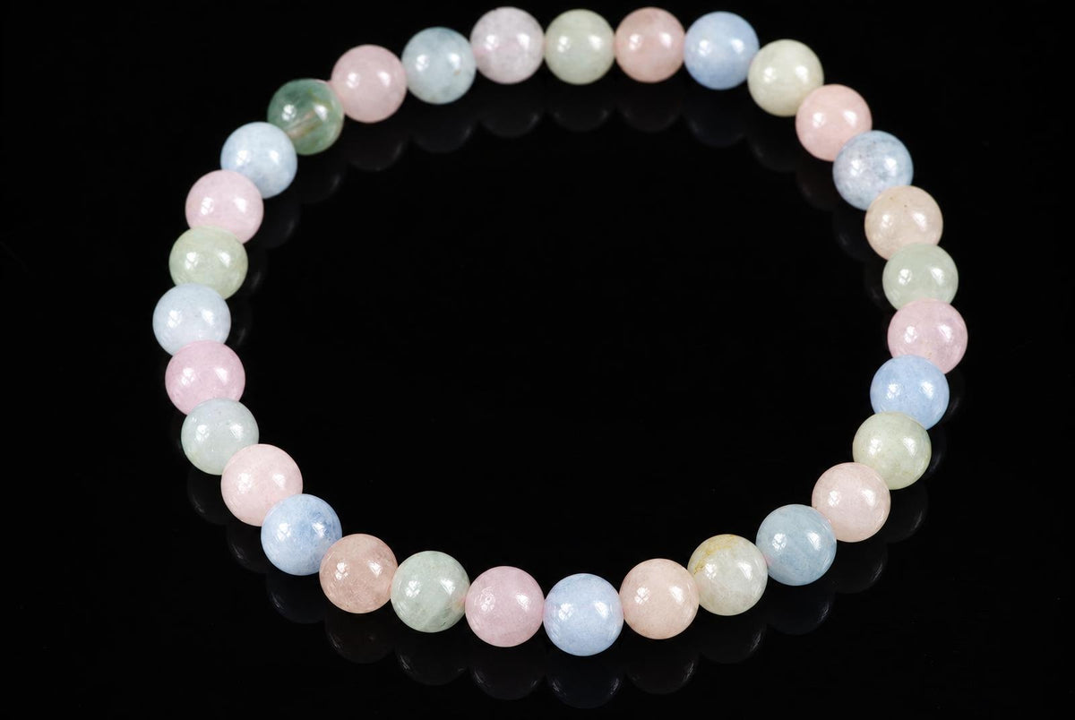 A bracelet of round beads in pastel pink, blue, green and cream colours on a dark surface.