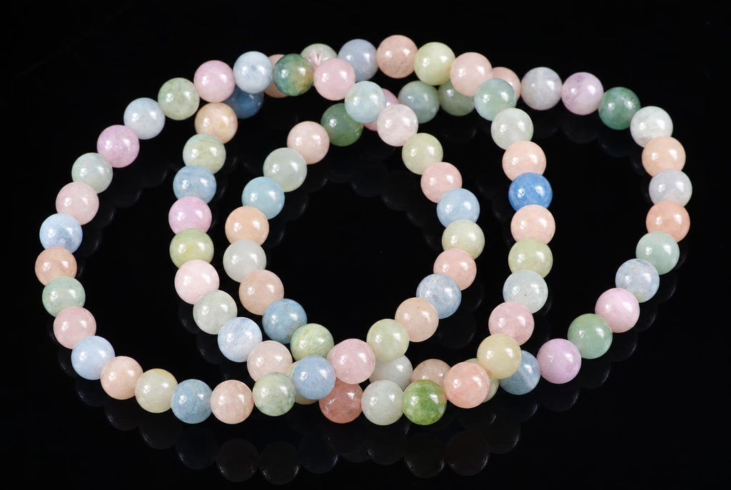 A beryl bracelet with round beads in pastel pink, blue, green and peach on a dark reflective surface.