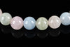 A row of round, polished beads in pastel pink, blue, green and white on a dark surface.
