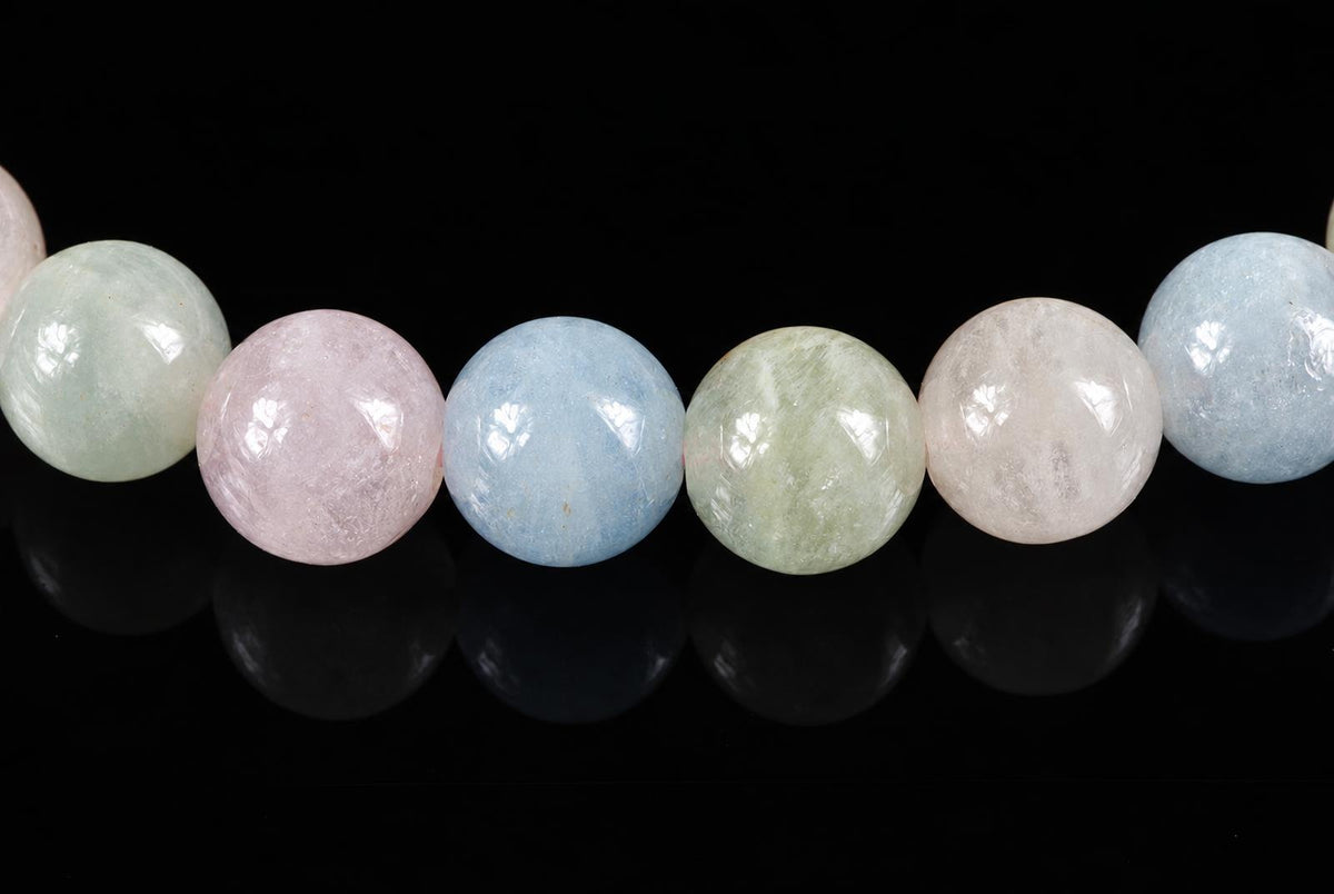 A row of round, polished beads in pastel pink, blue, green and white on a dark surface.