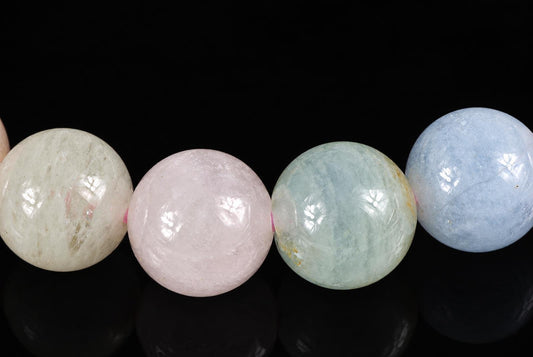 Four polished round beads in pale cream, pink, light green and blue on a dark surface.