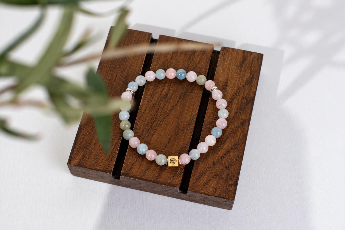 A beaded bracelet with pink, blue and pale green round beads on a dark wooden display stand.