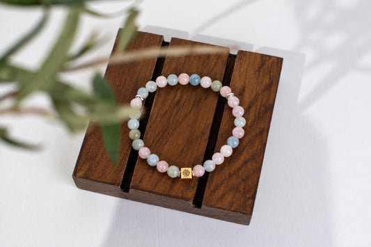 A beaded bracelet with pink, blue and pale green round beads on a dark wooden display stand.