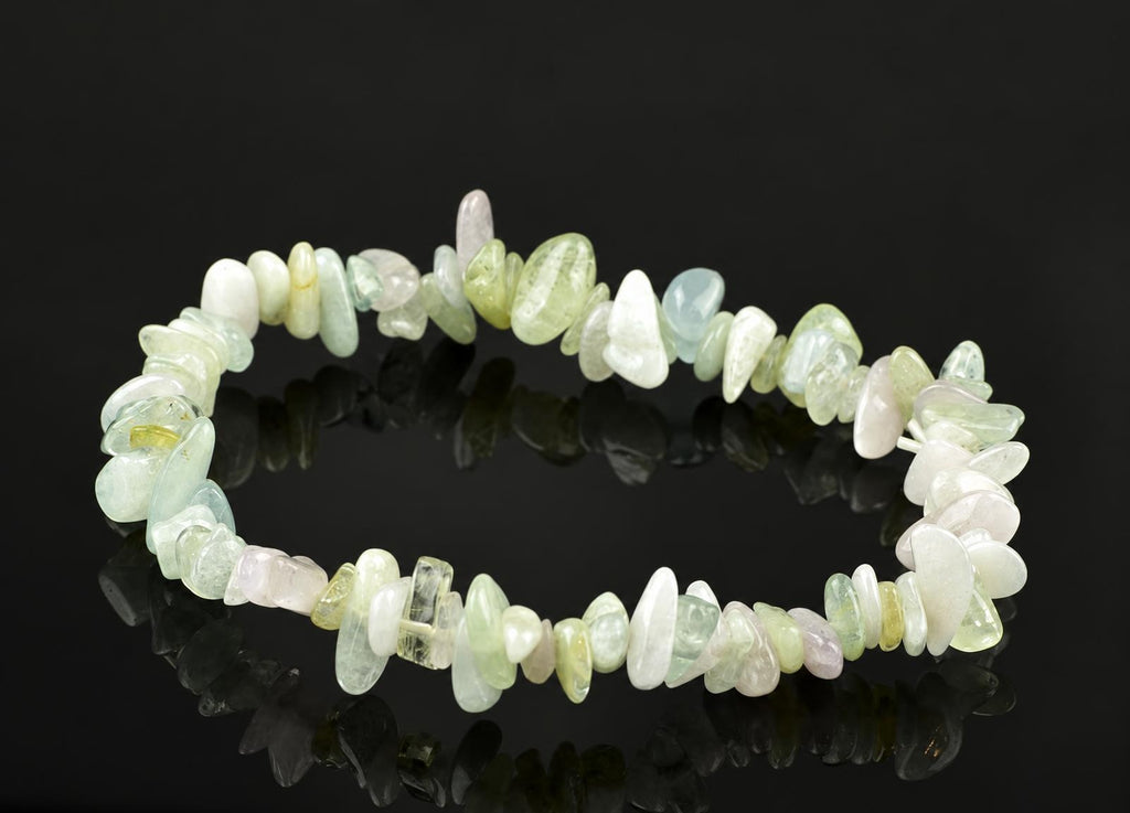 A beryl chip bracelet with pale green, white and pink stones on a dark reflective surface.