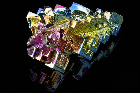 A cluster of iridescent bismuth crystals with metallic yellow, purple and blue facets on a dark surface.