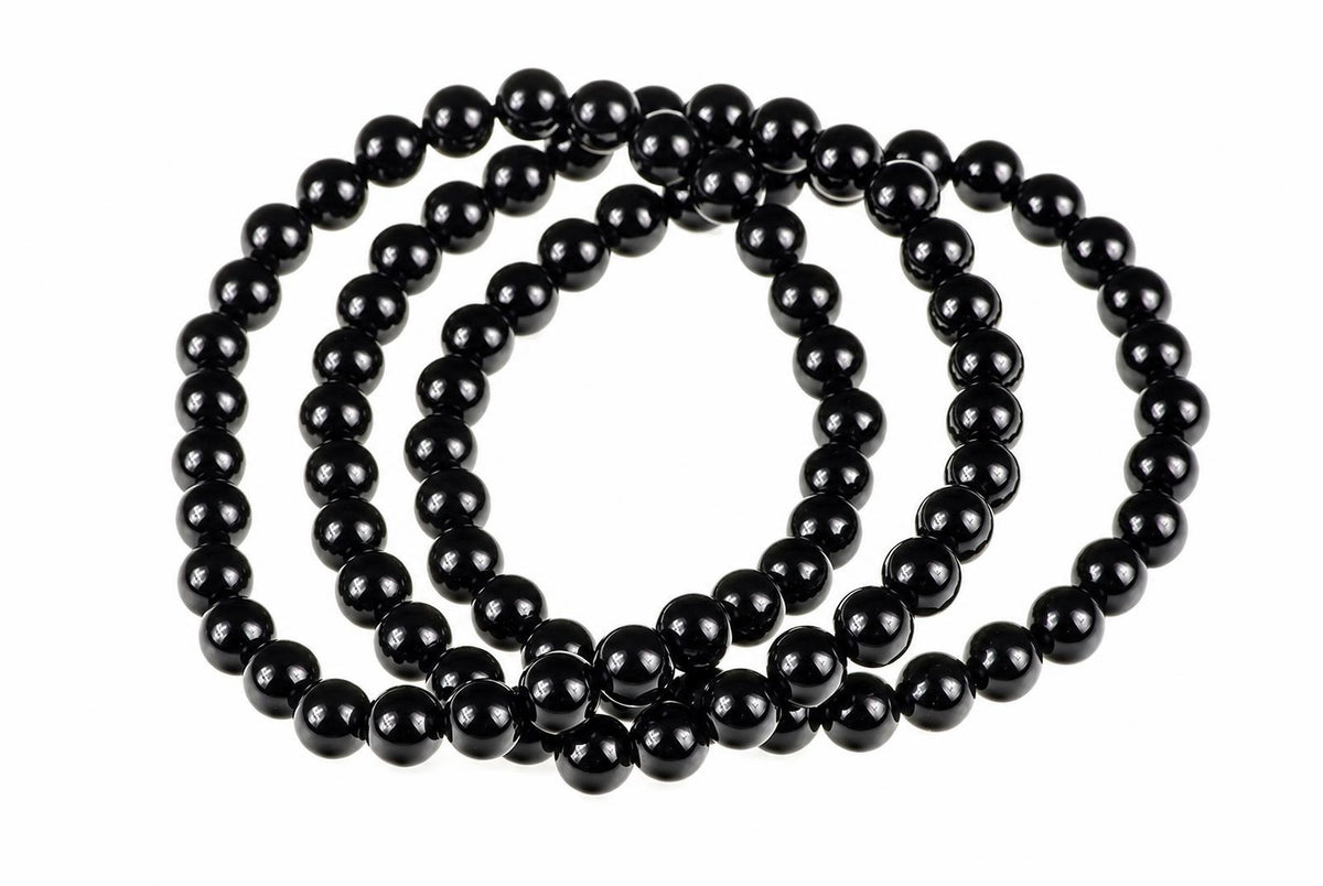 A black onyx bracelet with round beads arranged in a coil on a white surface.