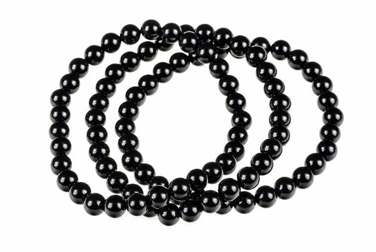 A black onyx bracelet with round beads arranged in a coil on a white surface.