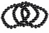 A black onyx bracelet with round beads arranged in a loop on a white surface.
