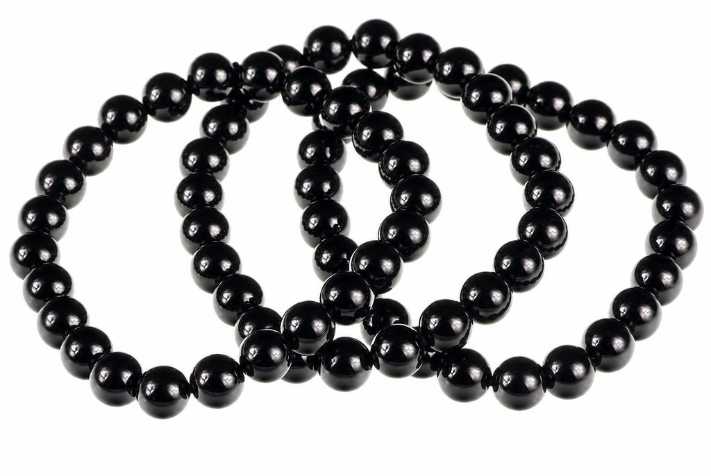 A black onyx bracelet with round beads arranged in a loop on a white surface.