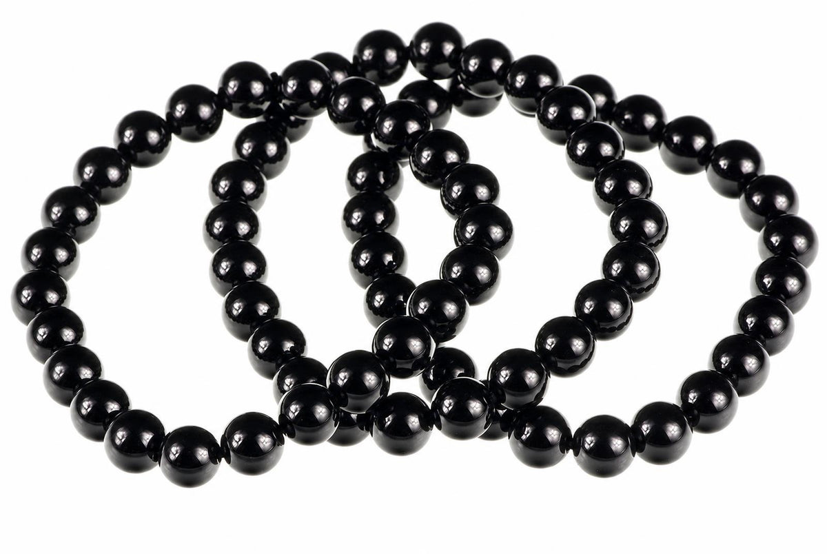 A black onyx bracelet with round beads arranged in a loop on a white surface.