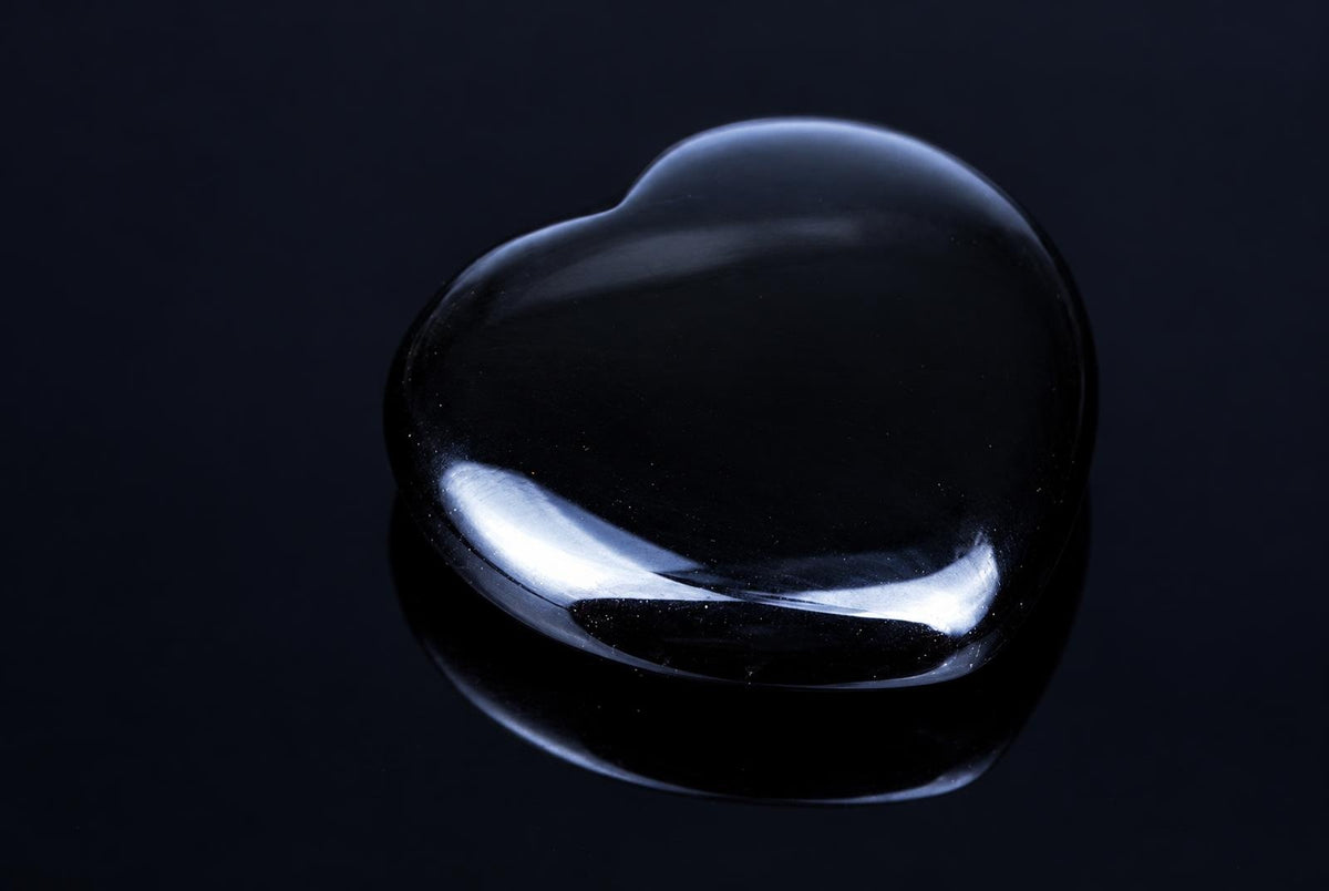 A polished, heart-shaped black stone with a smooth, reflective surface sits on a dark background.