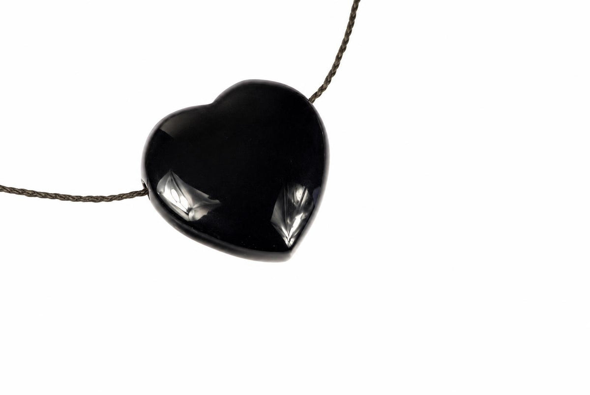 A glossy black heart-shaped pendant hangs from a dark cord against a plain white background.